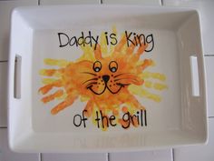 a white tray with an orange and yellow handprinted lion on it that says daddy is king of the grill