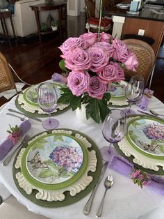 the table is set with pink roses in a vase and green china plates on it