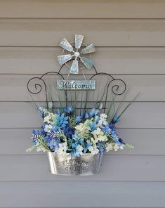 a metal bucket filled with blue and white flowers sitting on the side of a building