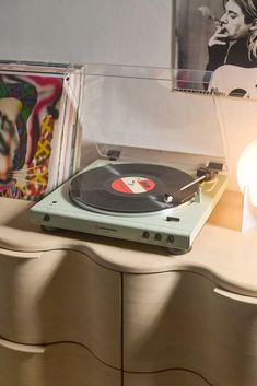 a record player sitting on top of a wooden dresser next to a lamp and pictures