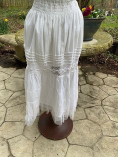 "Seashore? Sure! Picnic? Positively! This white 100% cotton skirt from ETC. in the 1980s is elasticized at the waist and has 4 rows of smocking just below the waistband.  Further down, you'll find 4 rows of pin-tucking followed by an insert of crochet lace.  At the bottom it's finished off with 2 tiers of soft net ruffles.  Lined to 24\" down.  In great condition.    Waist 28\" stretches to 50\" Hips 54\" Length 32\"" White Fitted Bottoms With Smocked Bodice, White Lined Petticoat For Spring, Beach Cotton Bottoms With Smocked Bodice, Beach Bottoms With Smocked Bodice In Cotton, White Tiered Skirt Petticoat For Summer, White Bottoms For Summer Garden Party, White Tiered Petticoat For Summer, Cotton Petticoat With Gathered Skirt For Daywear, Peasant Cotton Skirt For Spring