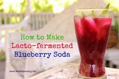 a tall glass filled with blueberry soda sitting on top of a table next to a white bench