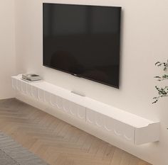 a flat screen tv mounted to the side of a white wall next to a plant