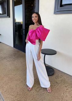 a woman standing in front of a door wearing white pants and a pink top with ruffles