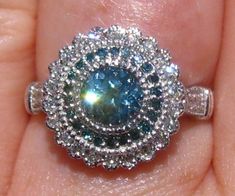 a close up of a person's hand holding a ring with a blue and white diamond