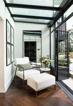 a white chair and ottoman in a room with glass walls, wood flooring and large windows