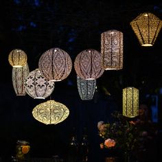 some lights that are hanging from the ceiling in front of a table with flowers and vases on it