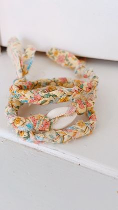 a close up of a flowered bracelet on a white surface with an object in the background