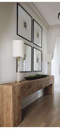 a wooden table with three pictures on the wall above it and a lamp next to it