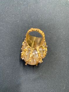 This vintage lady's showpiece ring is a true treasure. Made from 18k gold, it features a stunning oblong-shaped light yellow jade stone as the main attraction, accented by 58 white diamonds (.70 ct) and three emeralds (1 ct.). The patina light yellow color of the main stone adds a unique touch, while the intricate design of the ring makes it a true work of art. This ring is a size 5 and is branded by D.A.T, signed by Nuvill making it a must-have for any fine jewelry collection. Total weight 36+ grams. All measurements are approximated. One of the smaller emeralds reveals a chip upon close inspection. Luxury Gold Diamond Ring Collectible, Gold Gemstone Rings For Evening, Luxury Yellow Rings For Collectors, Unique Yellow Gold Dome Ring For Formal Occasions, Exquisite Gold Rings For Evening, Elegant Yellow Cabochon Rings, Luxury Gold Dome Ring With Cabochon, Elegant Oval Dome Ring Collectible, Unique Gold Oval Diamond Ring