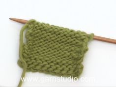 a green knitted object with a wooden knitting needle