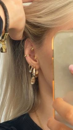 a woman with blonde hair is looking at her cell phone and wearing gold ear rings