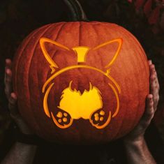 a person holding up a pumpkin with an image of a cat on it's face