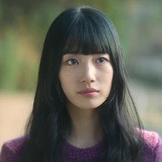 a woman with long black hair and bangs looking at the camera while wearing a purple sweater