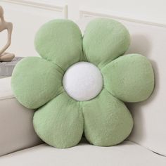 a green flower shaped pillow sitting on top of a white couch next to a statue