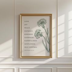 a white wall with a gold frame hanging on it and a green flower in the middle