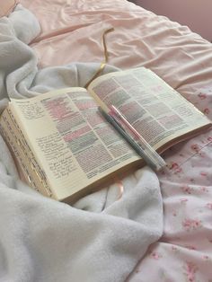 an open book laying on top of a bed next to a pen and pillow with pink flowers