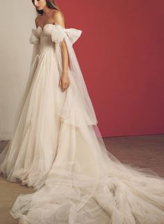 a woman in a white wedding dress standing against a red wall