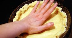 a person's hand on top of a pie crust in a glass dish pan