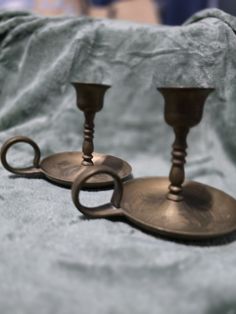 two metal candlesticks sitting on top of a blanket