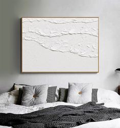 a large white painting hanging on the wall above a bed with pillows and throw blankets