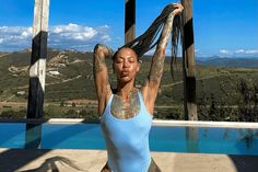 a woman in a blue tank top doing yoga by a pool with her hands up