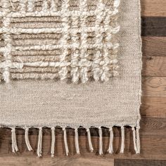 an area rug with fringes on top of wood flooring and a wooden wall