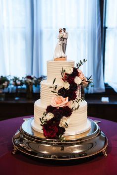 a white wedding cake with red and pink flowers on the top is sitting on a silver platter