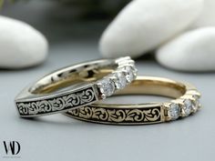 two gold wedding bands with diamonds on them sitting next to some rocks and white stones