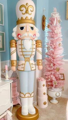 a large nutcracker standing next to a pink christmas tree in a blue room