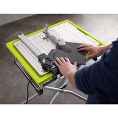 a person is using a table saw to cut paper on a green and white tray