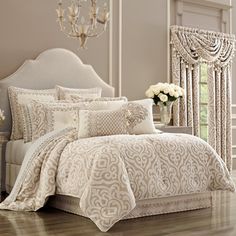 a white bed sitting in a bedroom next to a chandelier and window with curtains