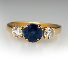 This beautiful ring is centered with one (1) round mixed cut natural sapphire set into a four-prong setting. The center stone is flanked to each side by one (1) round brilliant cut diamond set into a four-prong setting. The ring measures 5.9mm at the top, rises 5.5mm above the finger, tapering to 1.3mm wide and 0.7mm thick at the base of the shank. This ring is currently a size 5. Blue Sapphire Three Stone Ring With Diamonds, Classic Sapphire Ring With Lab-created Gemstone, Elegant Three-stone Sapphire Ring, Luxury Three Stone Sapphire Ring, Yellow Gold Three-stone Sapphire Ring, Yellow Gold Three Stone Sapphire Ring, Classic Cubic Zirconia Sapphire Ring, Fine Jewelry Sapphire Birthstone Ring With Brilliant Cut, Three Stone Sapphire Round Ring Fine Jewelry