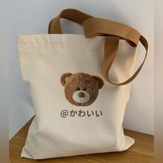 This Adorable Street-Style Japanese Kanji Cute Teddy Tote Bag Is A Versatile Design That Combines Youthful Style With Practical Functionality, Making It A Perfect Companion For Everyday Use. The Photo Embossed Teddy Bear Image And The Lettering In Japanese Kanji Which Translates To The Word “@Cute” Perfectly Nails The Kawaii Aesthetic! Crafted From Durable Canvas, It Offers Ample Space For Carrying Essentials Like Books, Groceries, Or Everyday Items. 100% Canvas Kanji Lettering Spells “Cute” In Beige Pouch Canvas Bag For School, Casual Cream Shoulder Bag For School, Trendy Cream Canvas Bag For School, White Harajuku Canvas Bag For Everyday Use, Casual Bags With Cute Design For Gift, Casual Bags Suitable As Gifts, Cream School Pouch Bag, Casual Shoulder Bag With Cute Design For Everyday, White Harajuku Shoulder Bag For Everyday