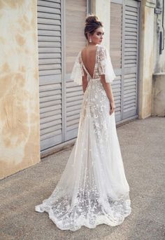 a woman in a wedding dress standing on the sidewalk with her back to the camera