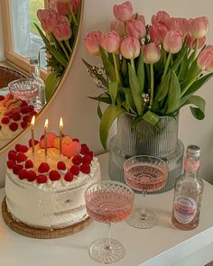 a white cake sitting on top of a table next to two wine glasses and a vase filled with flowers