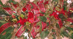 a christmas wreath with red and green ribbons on it's sides, surrounded by greenery