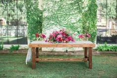 a wooden bench with flowers on it in front of a wall and grass area outside