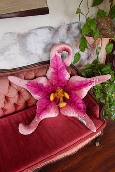 a pink flamingo shaped pillow sitting on top of a red couch next to a potted plant