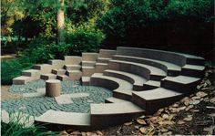 an outdoor seating area in the middle of a park with steps and trees around it