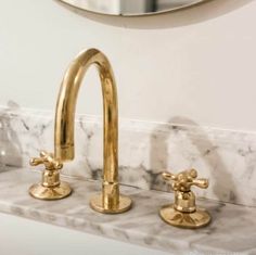 two gold faucets are sitting on a marble counter in front of a mirror