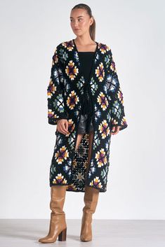 a woman standing in front of a white background wearing a black floral coat and boots