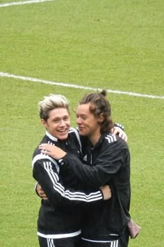 two young women hugging each other on a soccer field with grass and white lines in the background