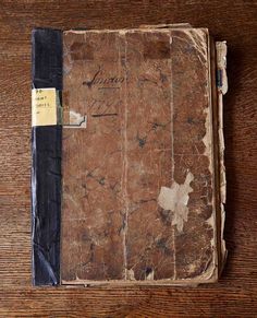 an old book with writing on it sitting on top of a wooden table next to a pen