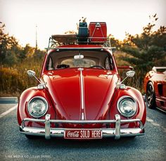 an old red vw bug with luggage strapped to it's roof is parked in a parking lot