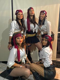 four women dressed up in pirate costumes posing for a photo together, with one woman sitting on the floor