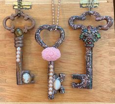 three key shaped pendants on a wooden surface with pearls and other items attached to them