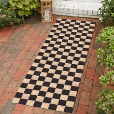 a black and white checkered rug sitting on top of a brick floor next to plants