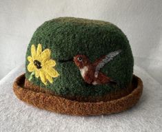 A felted alpaca hat highlighted by popular HUMMINGBIRDS The needle felt art can highlight the front, side or back, however you want to wear it. You can wear it with a curled brim or a flat brim. THE HATS ARE HAND KNIT FROM 1 STRAND OF BABY ALPACA FOR SOFTNESS AND ONE STRAND OF WOOL FOR SHAPE. They are then felted and finally needle felted MY FELTED HATS ARE ADJUSTABLE  AND FIT--20"--23.5' (SMALL-LARGE CIRCUMFERENCE). IF THE HAT FEELS A LITTLE LOOSE, YOU CAN TIGHTEN IT BY PULLING ON THE INSIDE BUTTON AND STRING AND RE-TYING. IF THE HAT FEELS A LITTLE TIGHT, YOU CAN REMOVE THE STRING COMPLETELY. Needle Felting Hat, Spring Wool Felt Hat, Adjustable Felt Cloche Hat, Adjustable Wool Cloche Felt Hat, Wet Felted Hats, Needle Felt Art, Felted Alpaca, Alpaca Hat, Felted Hats