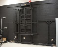 an empty room with black brick walls and metal bars on the wall, in front of a white refrigerator